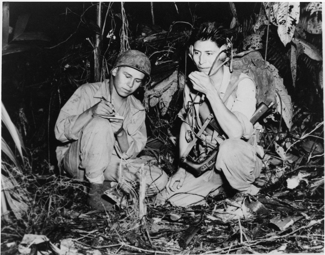 A black and white photograph of two soldiers crouching in a forest.