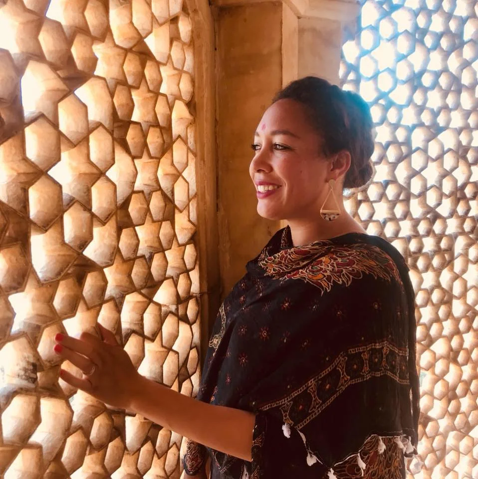 Courtney is pictured on a research trip to India, looking out of a latticed window with a beautiful traditional Indian dress and earrings.