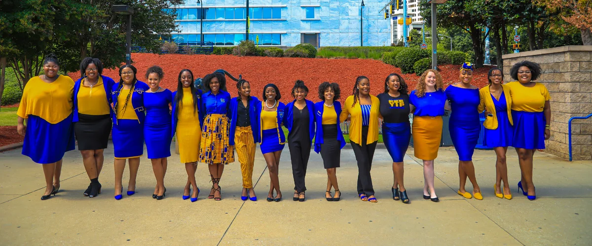 A group of 15 women wearing blue and white, standing in a line and smiling at the camera.