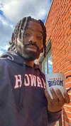 A man stands outdoors wearing a Howard sweatshirt and holding a Howard mug.