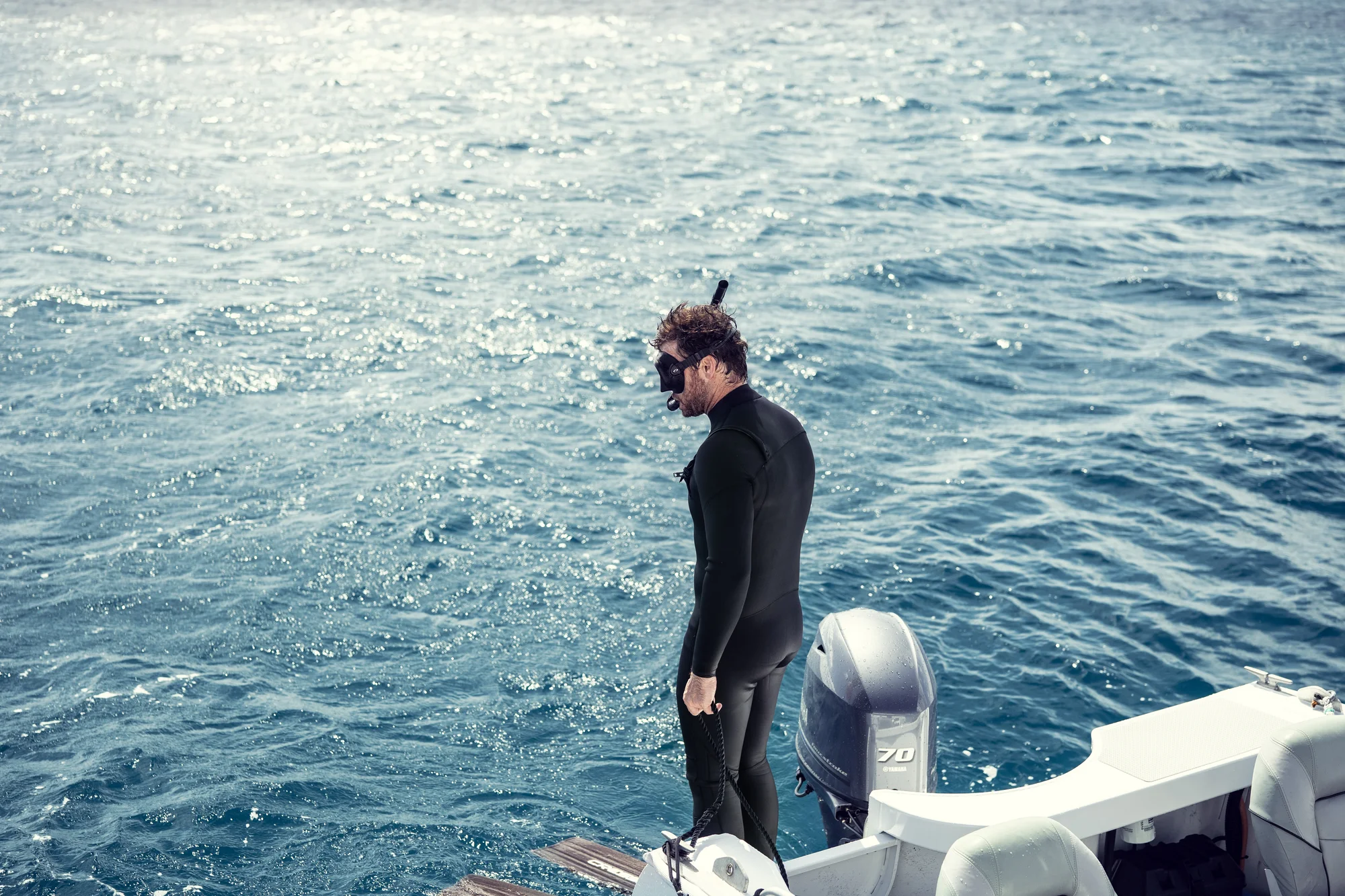 Johnny stands on the edge of the boat in a wetsuit, snorkeling gear and flippers.