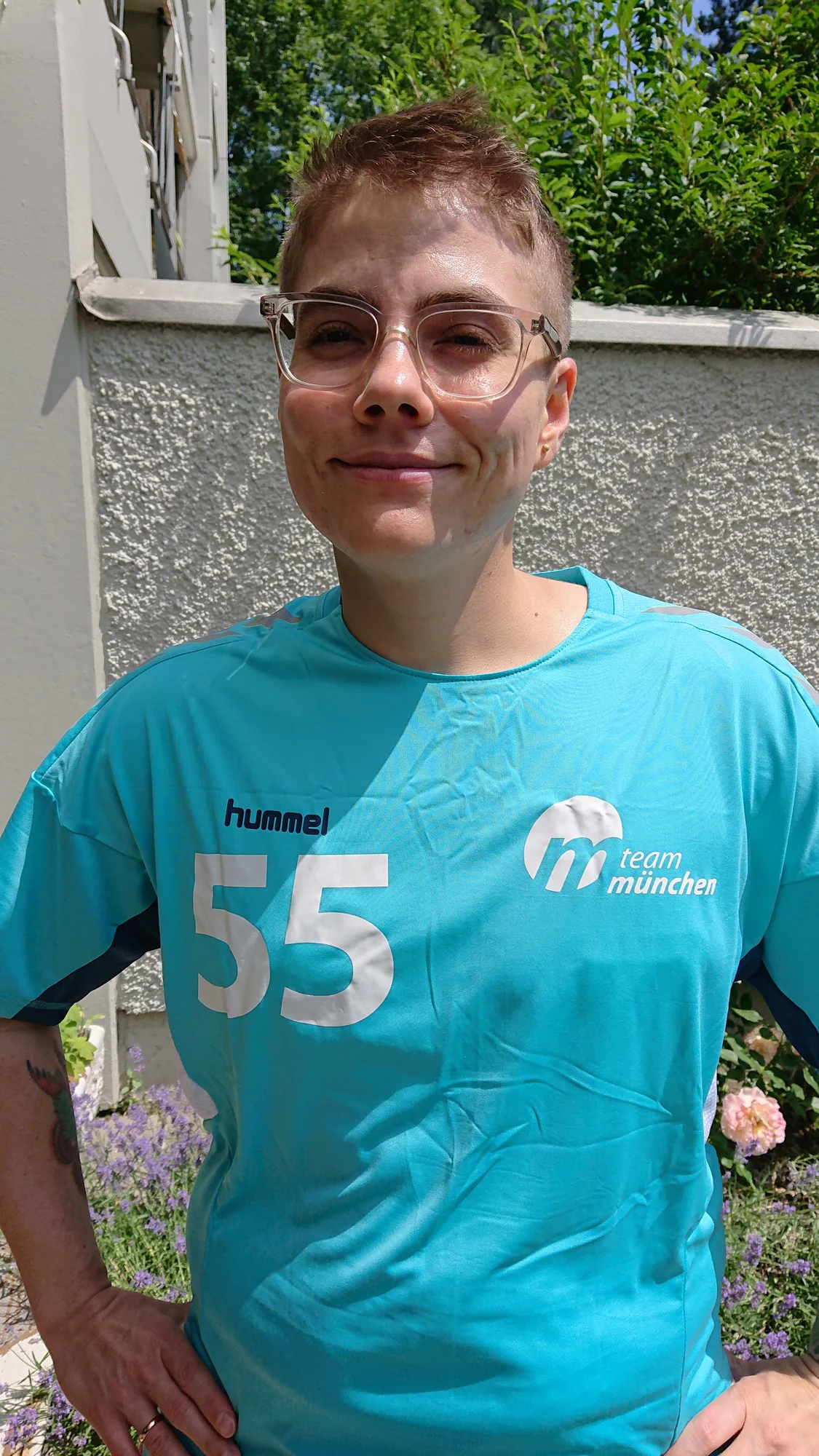 Adrian Hausner steht vor einer Mauer und trägt ein T-Shirt der Handballmannschaft von Team München