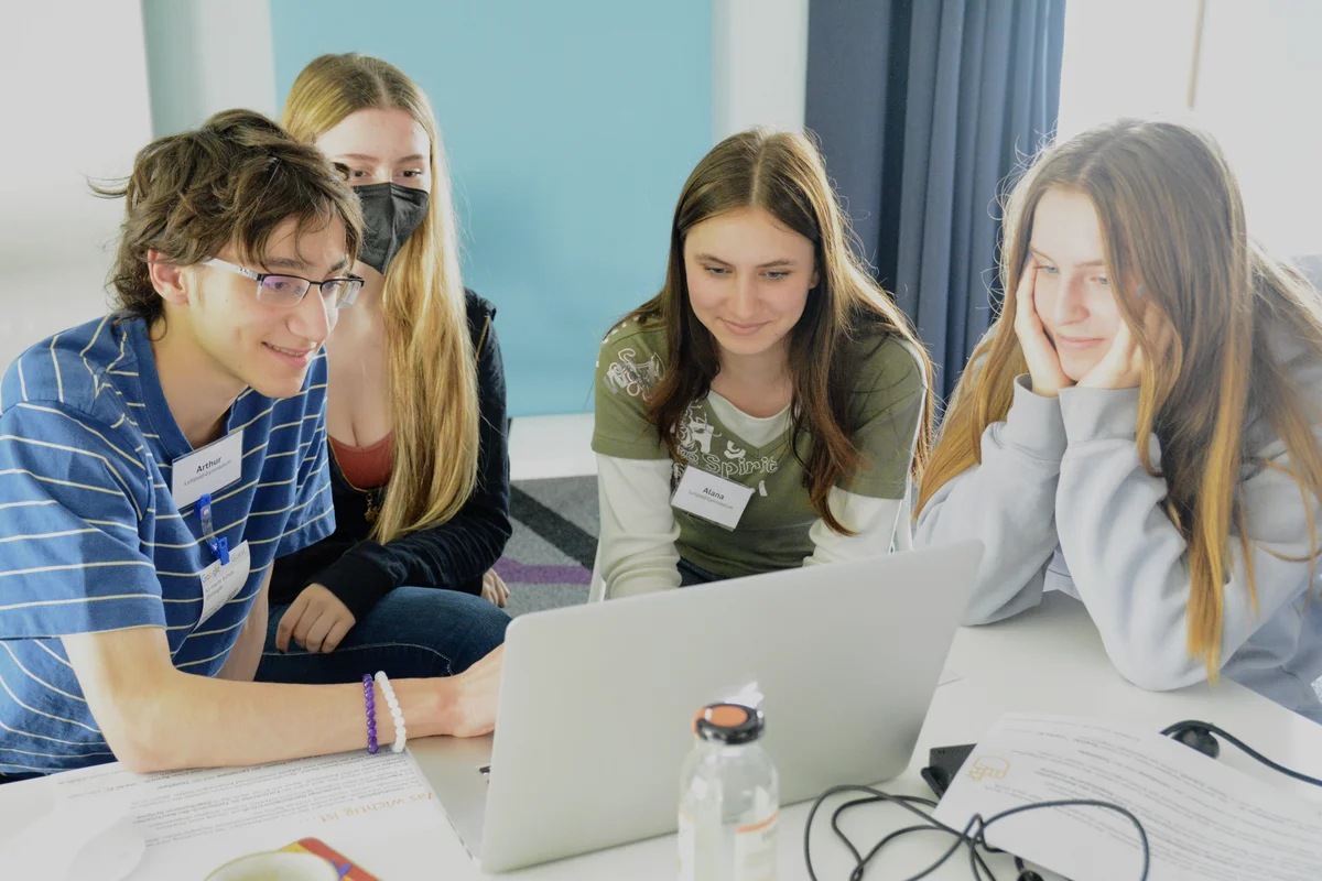 Foto auf dem vier Jugendliche vor einem Laptop sitzen und gemeinsam eine Aufgabe lösen