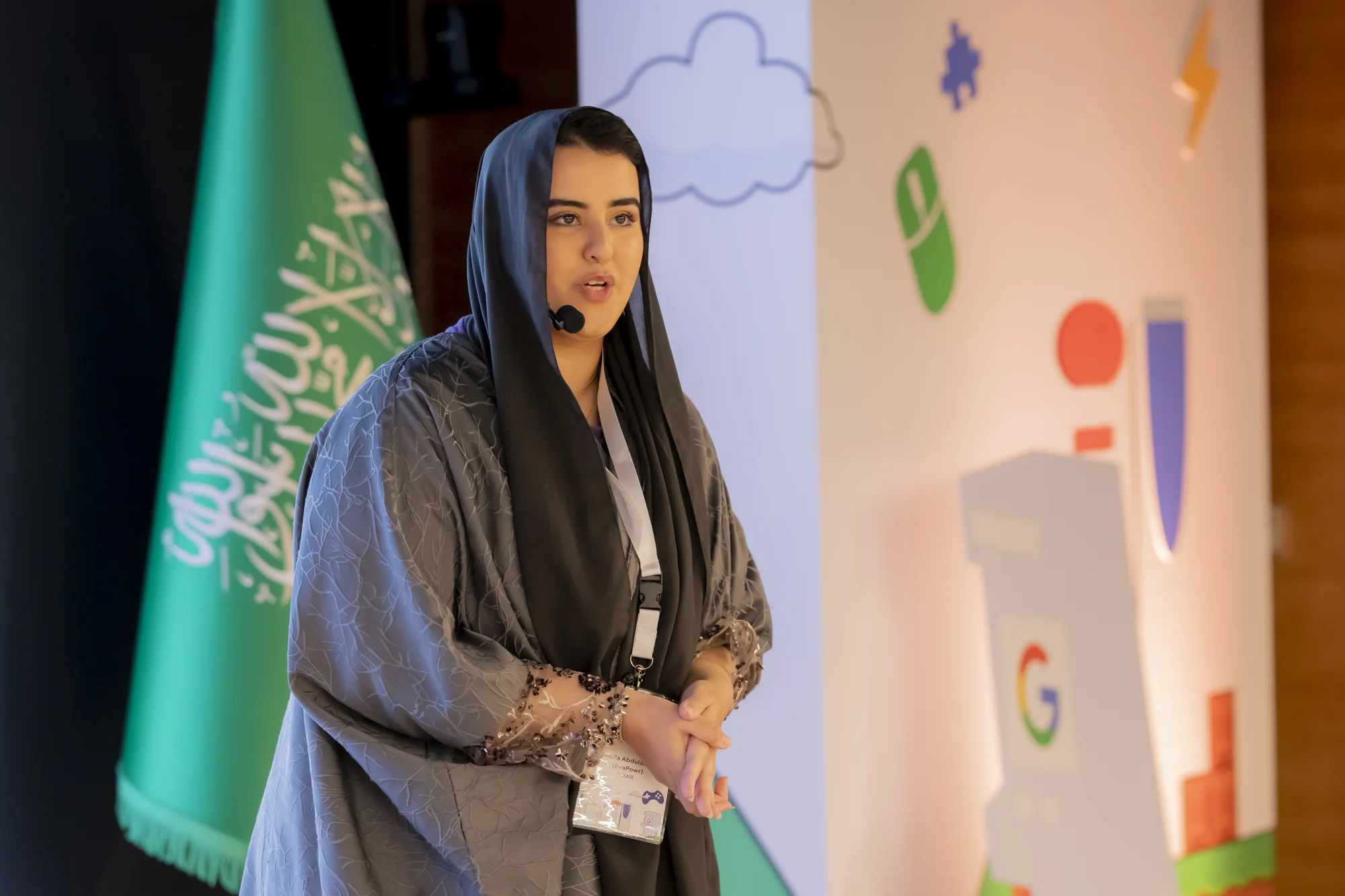 A picture of Haifa Abdulaziz (POWREVA) a content creator, wearing a grey abaya and scarf , presenting a lightening talk at yesterday's Google Gaming Forum
