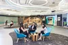 Three people sitting in chairs in a contemporary looking office space, chatting. One of them is holding a laptop.