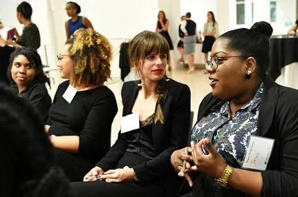 Four women wearing black and sporting nametags talking to one another.