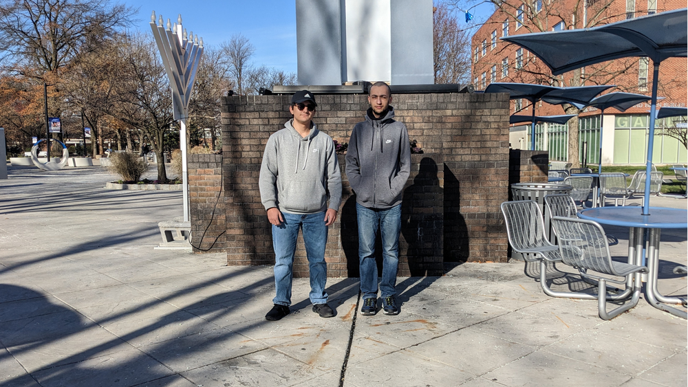 Eric and Xavier standing in front of a statue on campus of Kean University.
