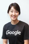 Smiling woman with black hair wearing a black shirt with the word Google printed on it in white text