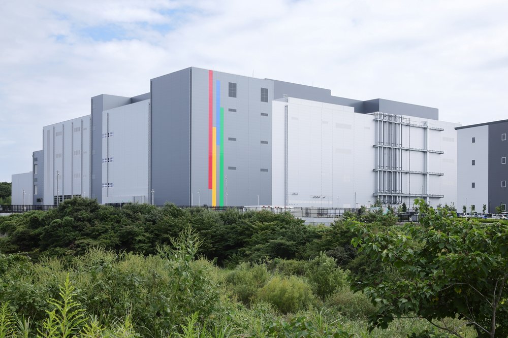 The exterior of Google’s data center, a wide gray building with grass and trees in the forefront.