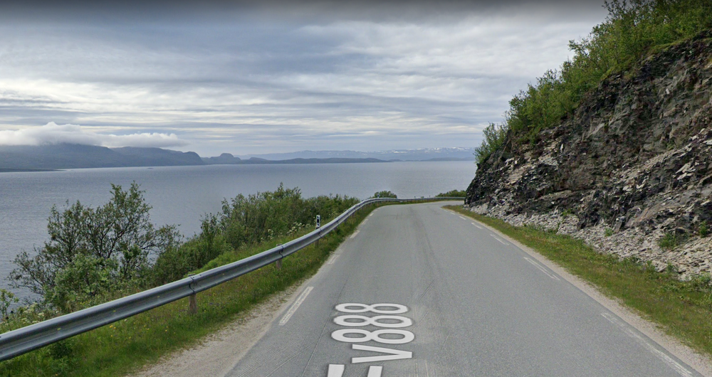 Image showing a road with cliff on one side and water on the other. Snow is off in the distance.