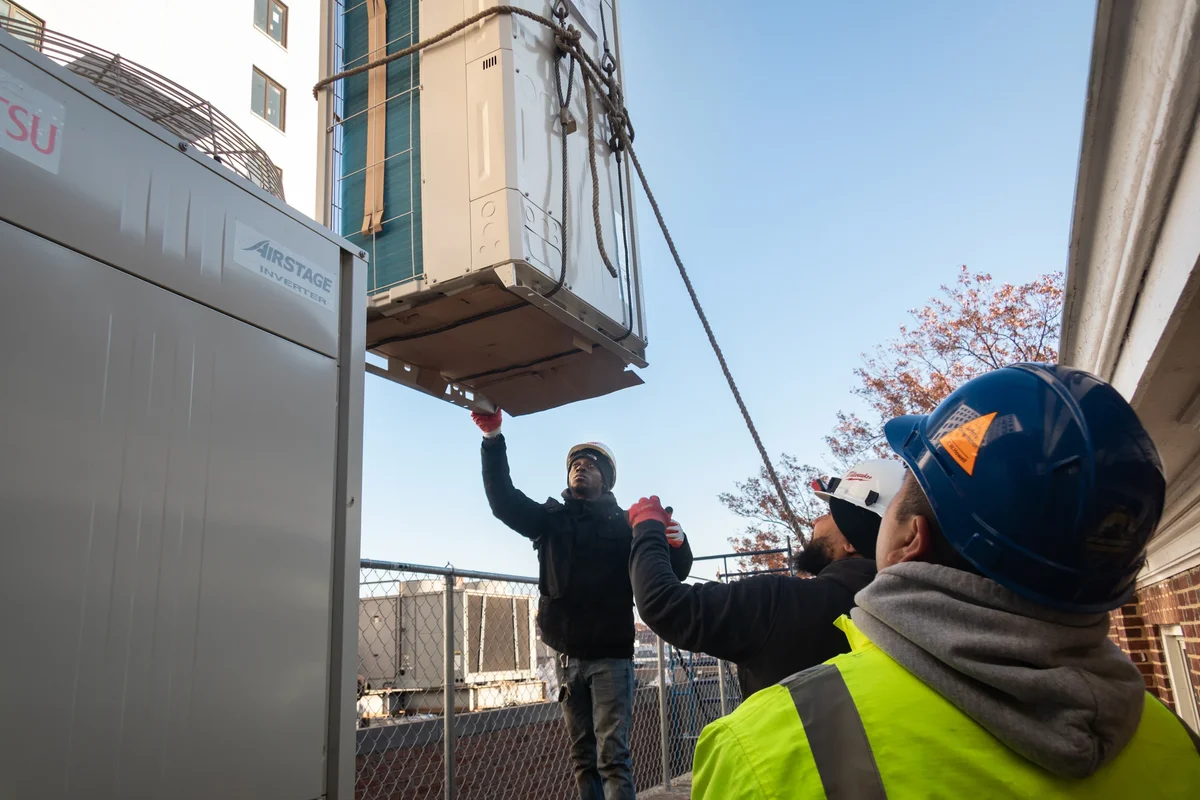 Two men wearing hard hats unload equipment from a crane.