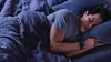 A man in bed sleeping, wearing a Fitbit device.