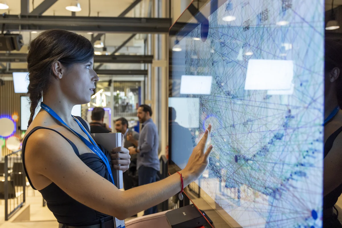 Photograph of a woman wearing a Google lanyard looking at a large screen in an office.