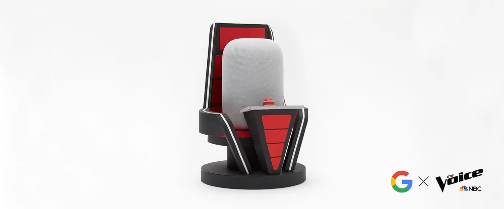 Image shows a Nest Audio device in a judges' chair from The Voice against a white background. The Google and The Voice/NBC logos are in the bottom right-hand corner.
