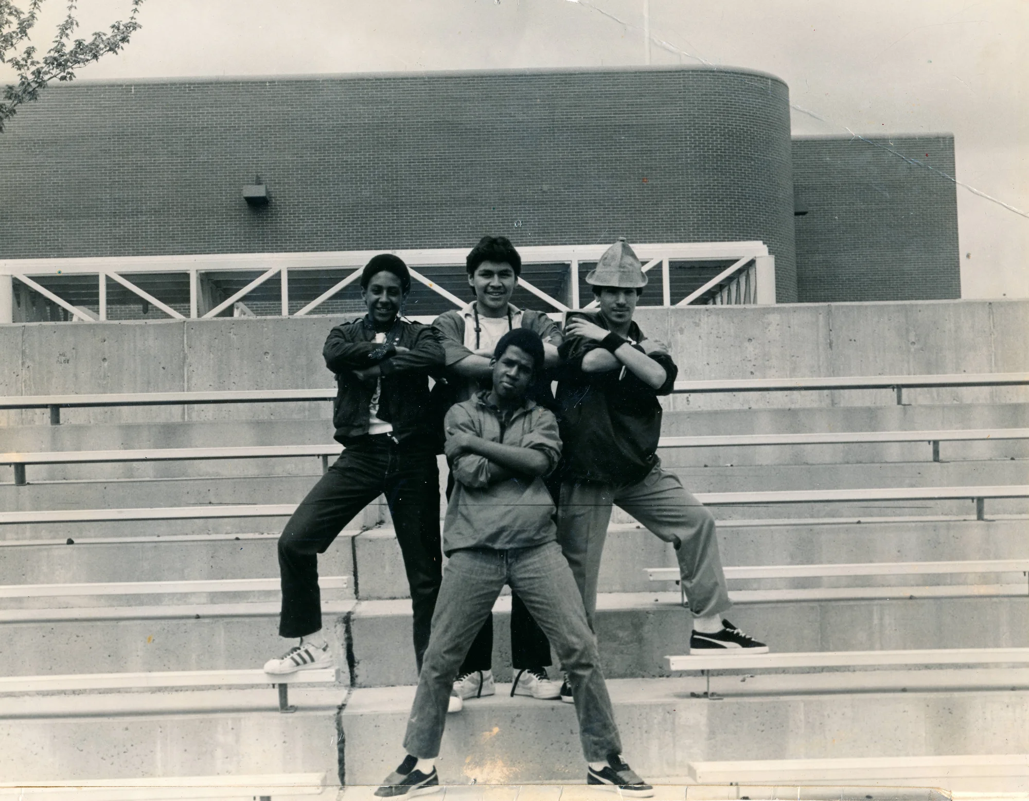 Black and white photograph of four men standing on steps, in front of a building, with their arms crossed.