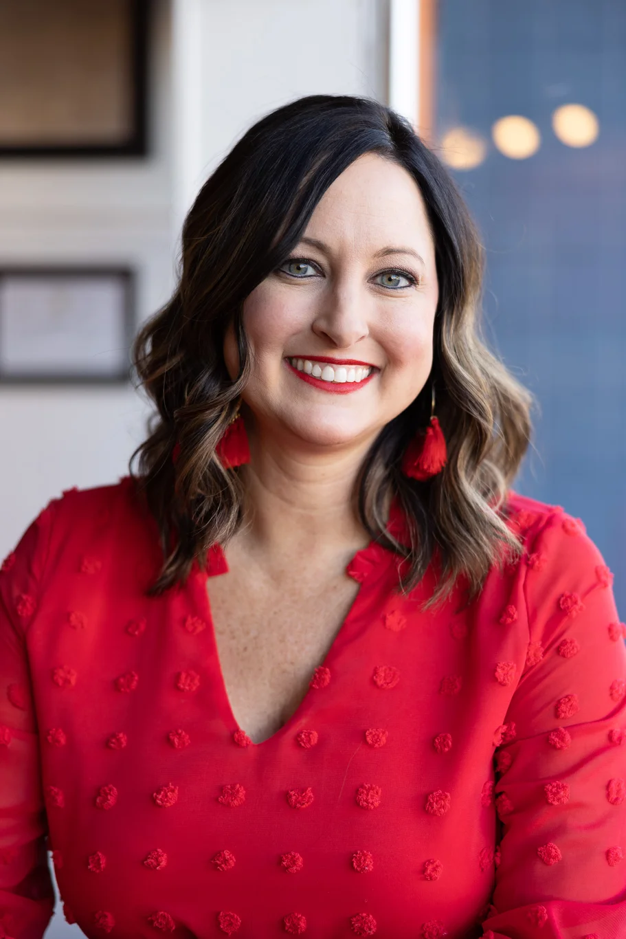 A woman wearing a red blouse smiles directly at the camera.