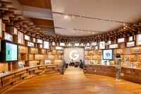 A photo of the interior of the Google Store with a woman looking at the Google hardware that's displayed. A lit up G is on the back wall.