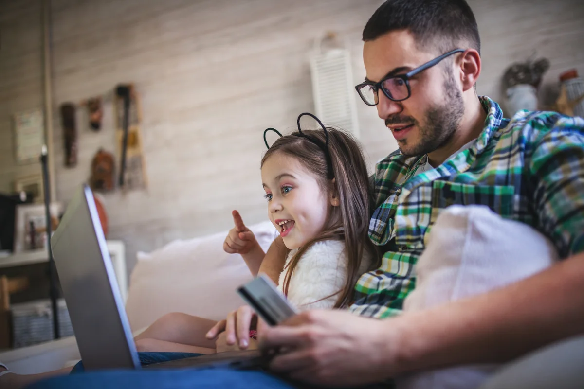 A father and daughter sitting on a couch, using a laptop to shop online.