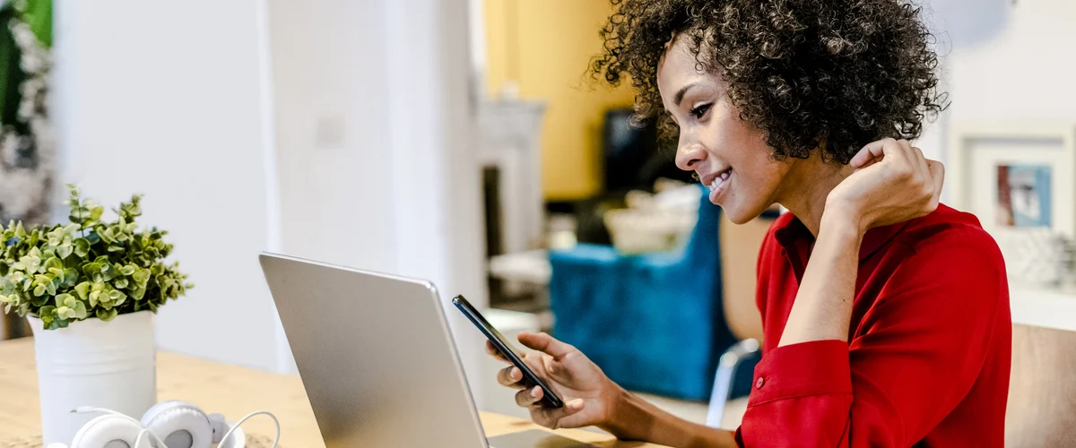 A woman sitting at a desk and looking at her phone while smiling.