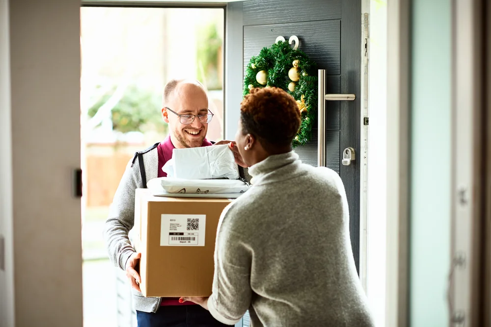 A person opens their door to receive a package from a delivery person.