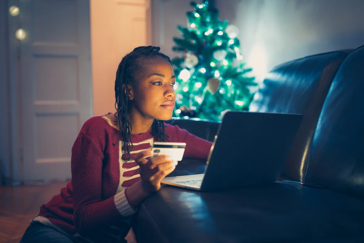 A woman holding up a credit card and looking at her laptop screen