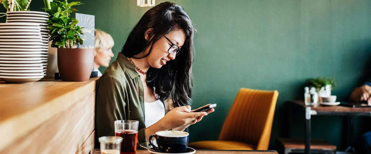 A woman smiling at her mobile phone while sitting in a restaurant.