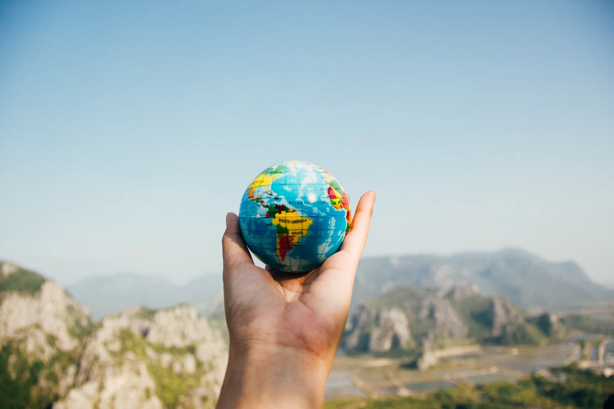 A hand his holding a small globe in front of a mountain