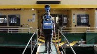 A photo showing Daniel Nadasi from behind, walking onto a green and yellow ferry wearing the blue Street View trekker backpack.