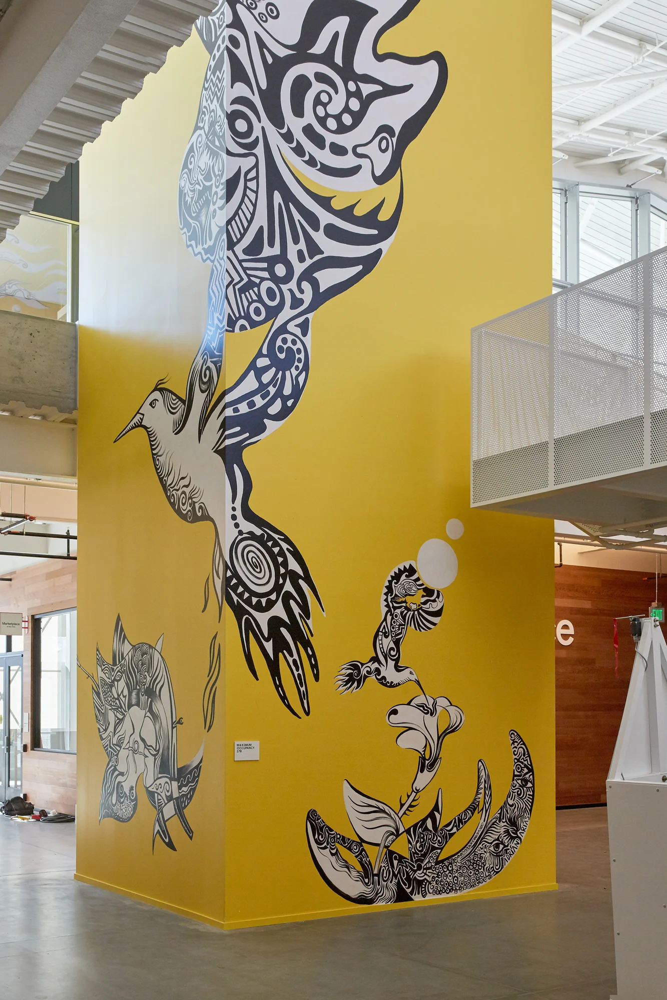 A photograph of the mural showing a yellow background with black and white drawings of hummingbirds.
