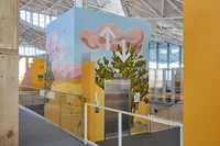 A photograph of Mariangela's mural. The mural shows a sky with pink, fluffy clouds and yellow grasslands and cartoonish green trees.