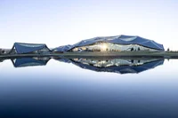 A water basin reflects the sun in front of two low round buildings at the Bay View campus.