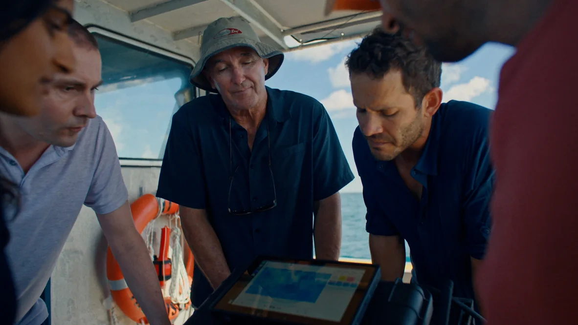 The CSIRO and Google team reviewing underwater imagery from the boat, looking at a screen showing detection of crown-of-thorn-starfish by the AI model