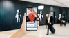 A still photo of a hand holding a phone showing the red map marker on the screen, in front of a bathroom entrance at the airport