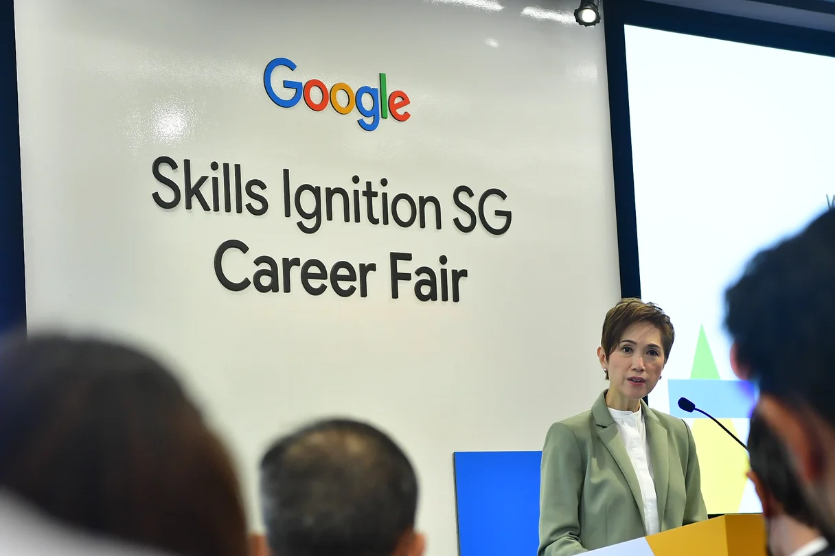 Photograph of person speaking at podium in front of an audience. Sign behind her reads: Google Skills Ignition SG Career Fair