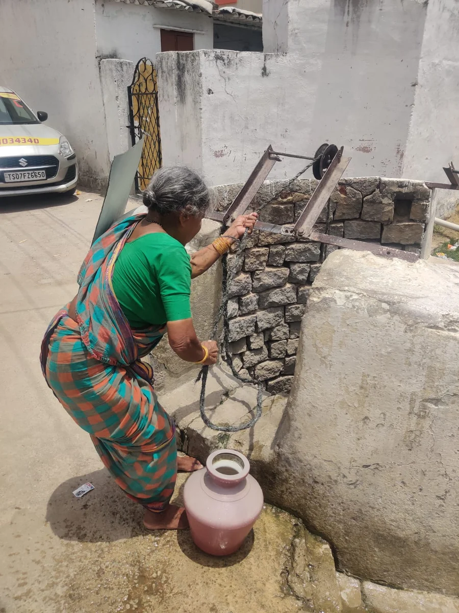 A woman bending down to retrieve water from a well.