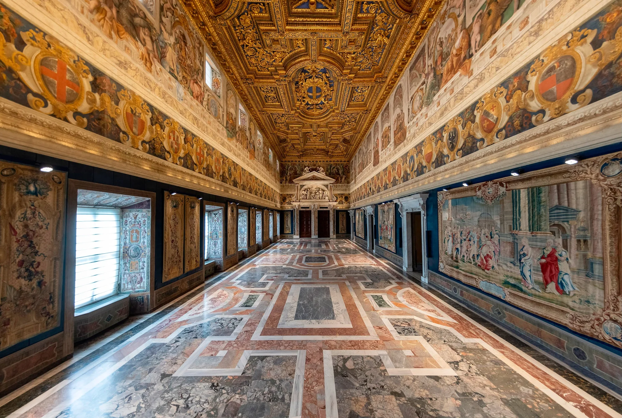 A hallway with colorful marble floor and richly decorated painted walls and ceilings.