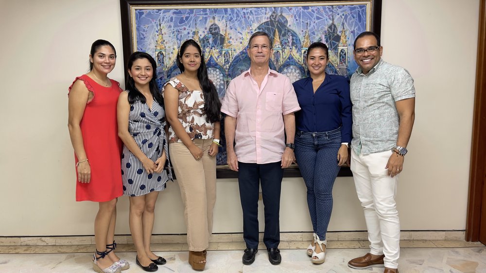 A group of four women and two men stand in front of a painting posing for the picture