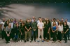 A group of about 30 people stand smiling at the camera in front of a gray wall.