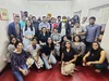 This picture shows The News Minute team. There are a group of people inside an office room. Some of the group are seated on the floor while others are standing behind them. There are 28 people visible. The room has white walls and the floor is a red color.