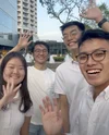 Four members (three men and one woman) of the HeadHome team are wearing white t-shirts and smiling and waving at the camera.