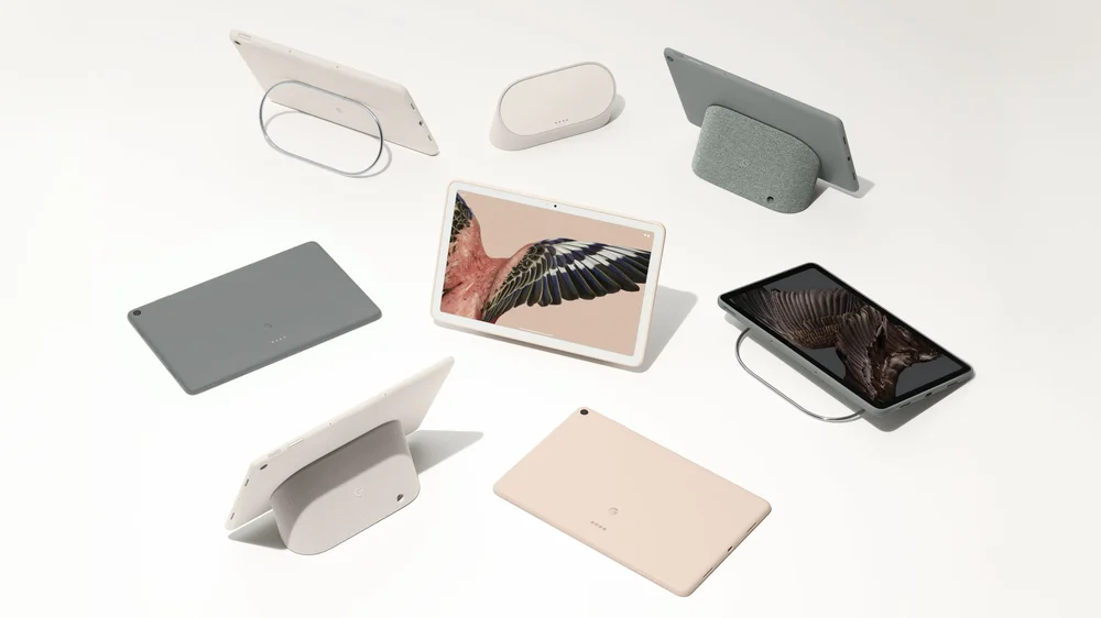 Overhead shot of seven Pixel Tablets in Porcelain, Rose and Hazel, two cases in Porcelain and Hazel and three Charging Speaker Docks.