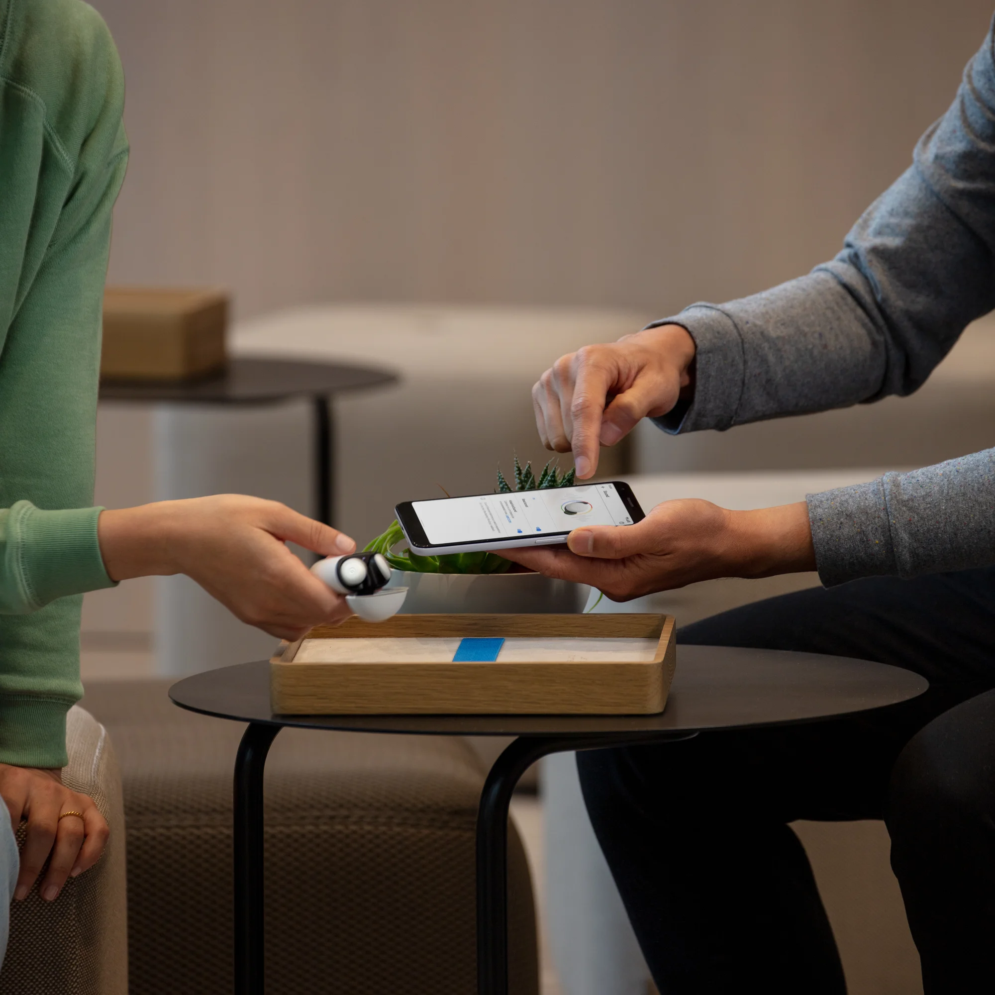 A person shows a Pixel phone to another person holding Pixel Buds.