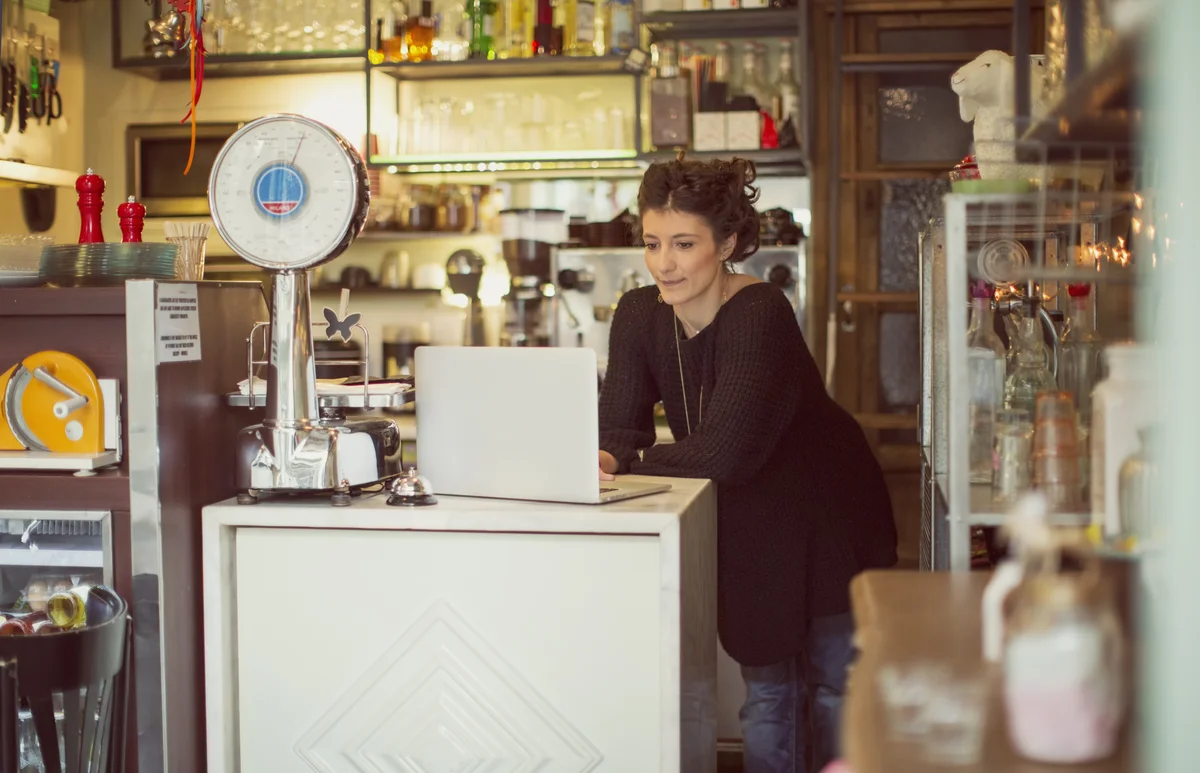 A coffee store owner working on a laptop at the shop counter