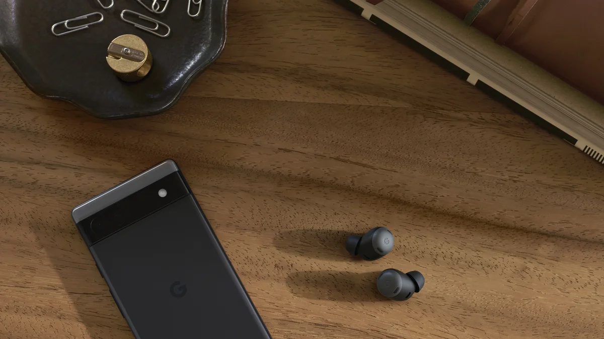 Ein Pixel 6a liegt auf dem Display links neben einem Paar Pixel Buds Pro auf einem Holztisch