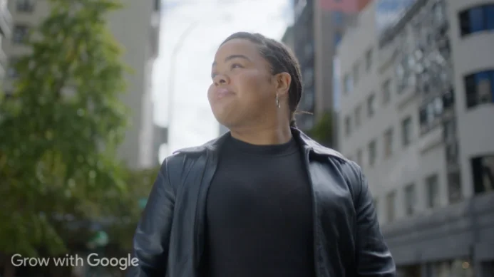 A woman in a black shirt and black jacket walks on a city street