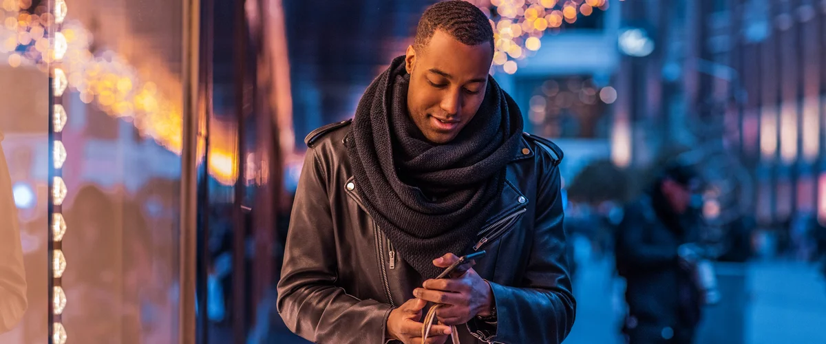 Man holding a shopping bag walking down the street and looking at his phone