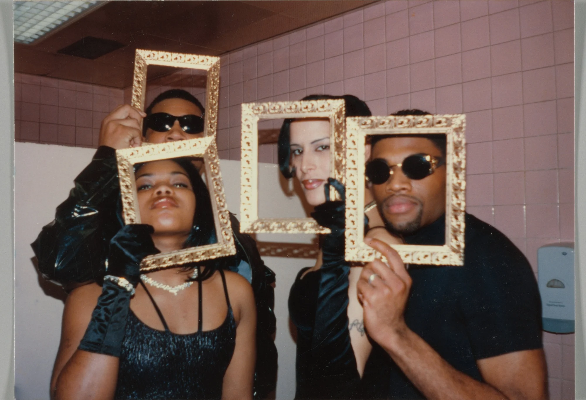 Four members of the House of Prestige, dressed in all-black ensembles, pose with ornate gold picture frames around their faces.