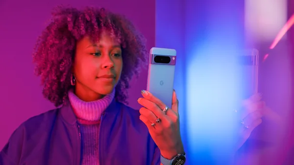 A woman is sitting up in bed. She is holding a Pixel 7 Pro in her left hand and looking at the screen with a slight smile.