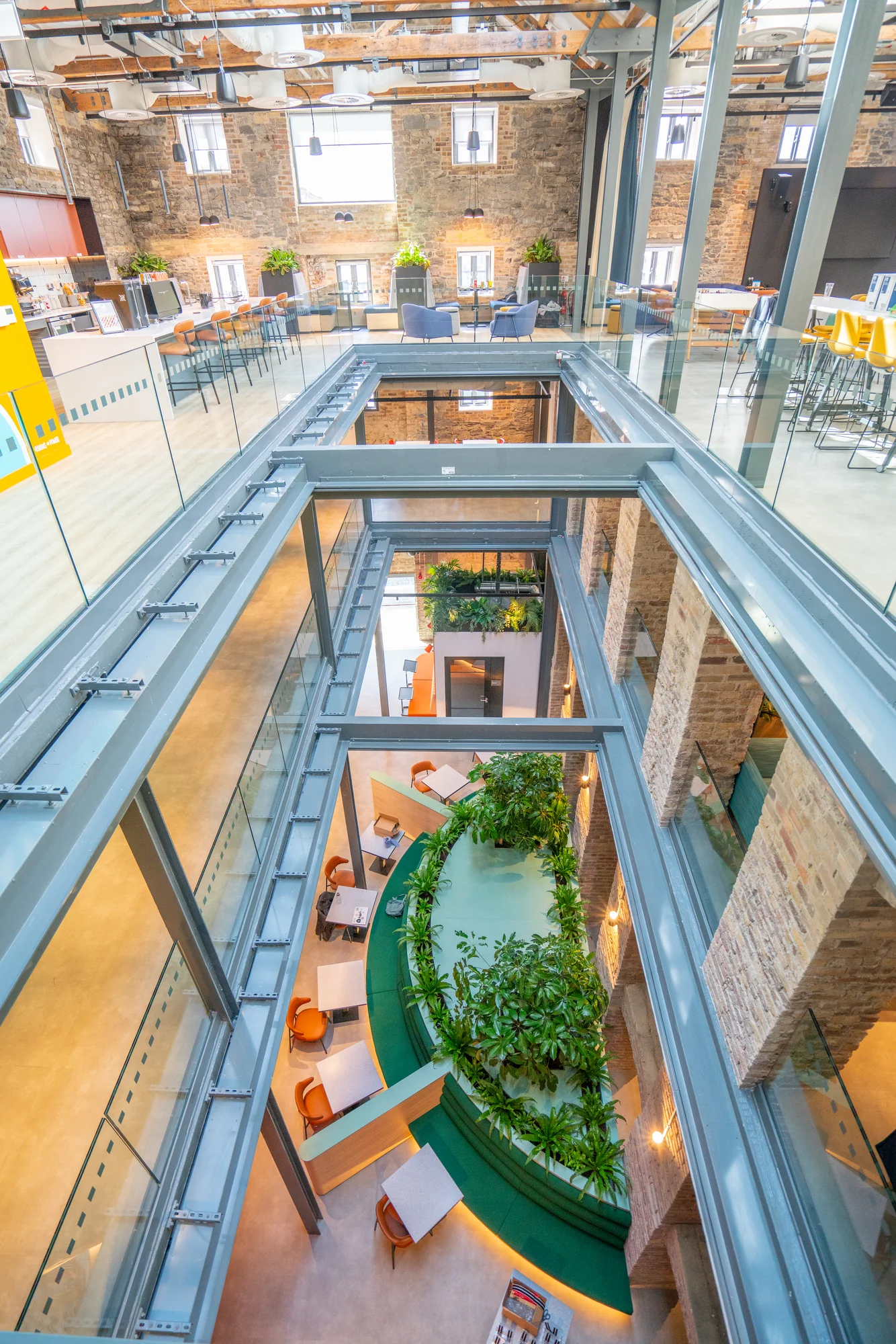 A large, open atrium showing exposed brick walls, seating areas and greenery.