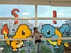 Kalaivani standing in front of a wall of post it art displaying the Pokemon, Charmander and Bulbasaur.